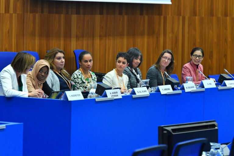 Des personnes assises à une table de conférence participent à un panel professionnel dans une salle aux boiseries murales.