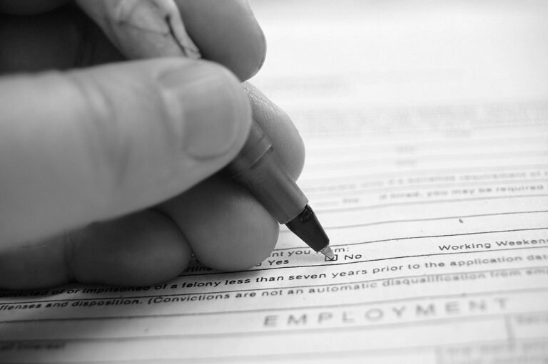 Gros plan en noir et blanc d’une main tenant un stylo au-dessus d’un formulaire papier comportant des cases à cocher et du texte imprimé.