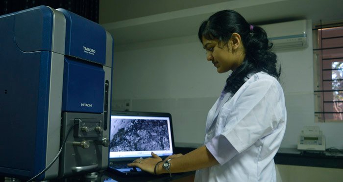 Une étudiante en blouse blanche utilise un appareil scientifique devant un ordinateur dans un laboratoire.