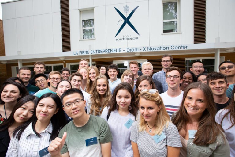 Groupe de jeunes adultes posant devant un bâtiment de l’École Polytechnique, identifié comme le Drahi-X Innovation Center.