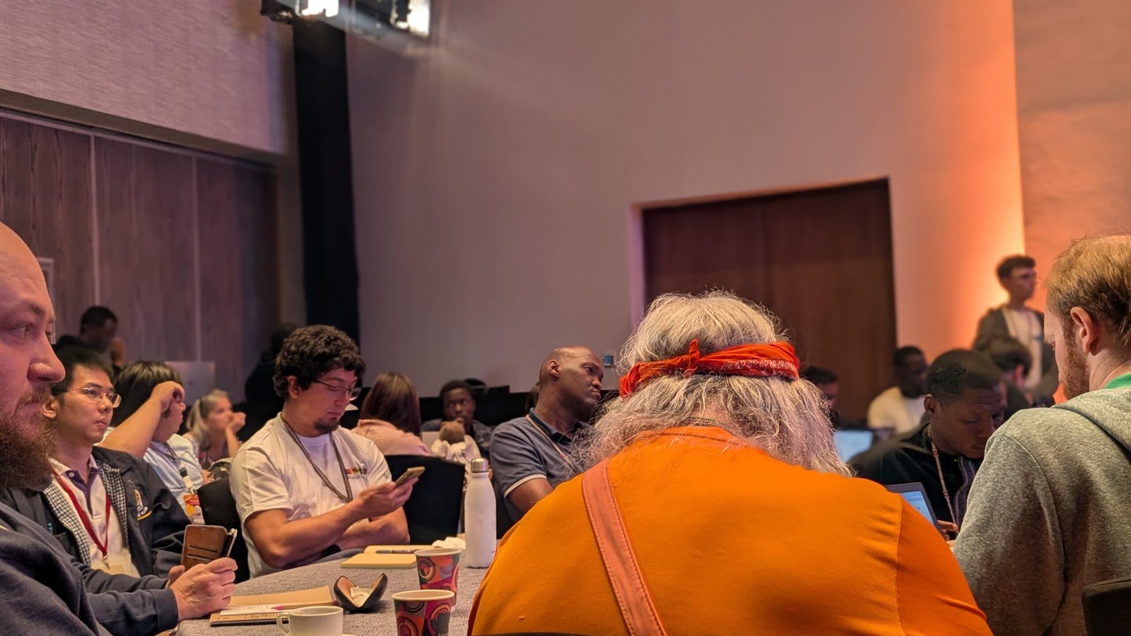 Des personnes réunies autour de tables dans une salle, certaines consultant un ordinateur, un téléphone ou des documents.