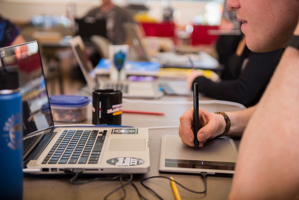 Des étudiants travaillent à une table avec des ordinateurs portables, des cahiers et du matériel d’écriture.