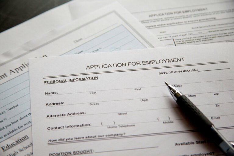 Des formulaires imprimés de candidature à l’emploi sont posés sur une surface, avec un stylo au premier plan.