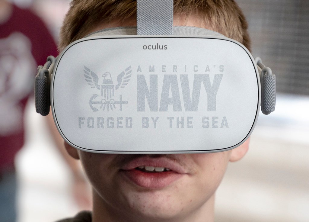 Gros plan d’une personne portant un casque de réalité virtuelle blanc marqué « America’s Navy » et « Forged by the Sea ».
