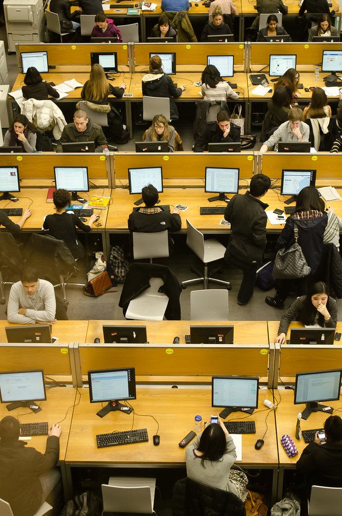 Vue en hauteur d’une salle d’étude avec plusieurs personnes assises à des bureaux équipés d’ordinateurs, de claviers et de documents.