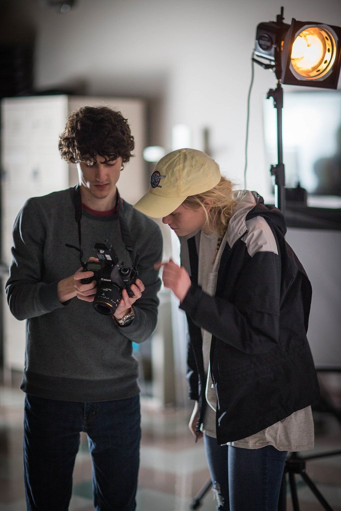 Deux jeunes personnes penchées sur un appareil photo, dans un studio éclairé par un projecteur.