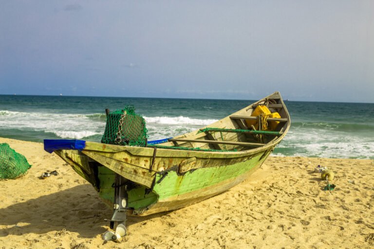 Une embarcation de pêche en bois repose sur une plage de sable, avec des filets et du matériel à bord, devant la mer.